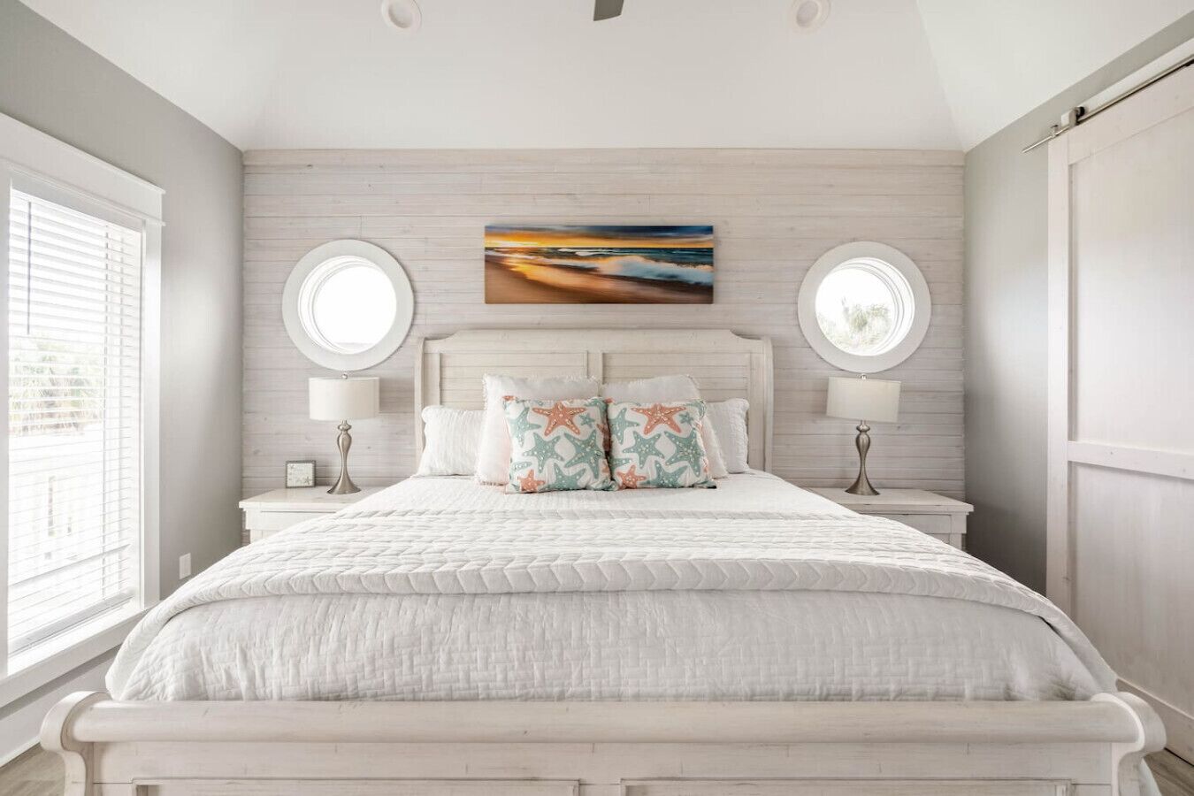 A bedroom with a large bed, two bedside tables, a round mirror, and a painting on the wall.