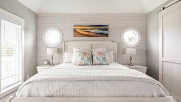A bedroom with a large bed, two bedside tables, a round mirror, and a painting on the wall.