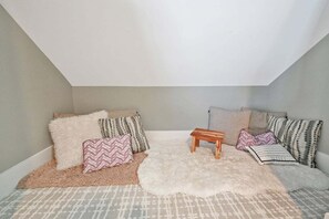 A cozy room with a sloped ceiling, a small wooden table, and a variety of patterned pillows. - Channel Marker: Exclusive Lakefront Home w/Hot Tub, Custom Bunk Room, Dock & Optional Boat Rental (Mooresville)