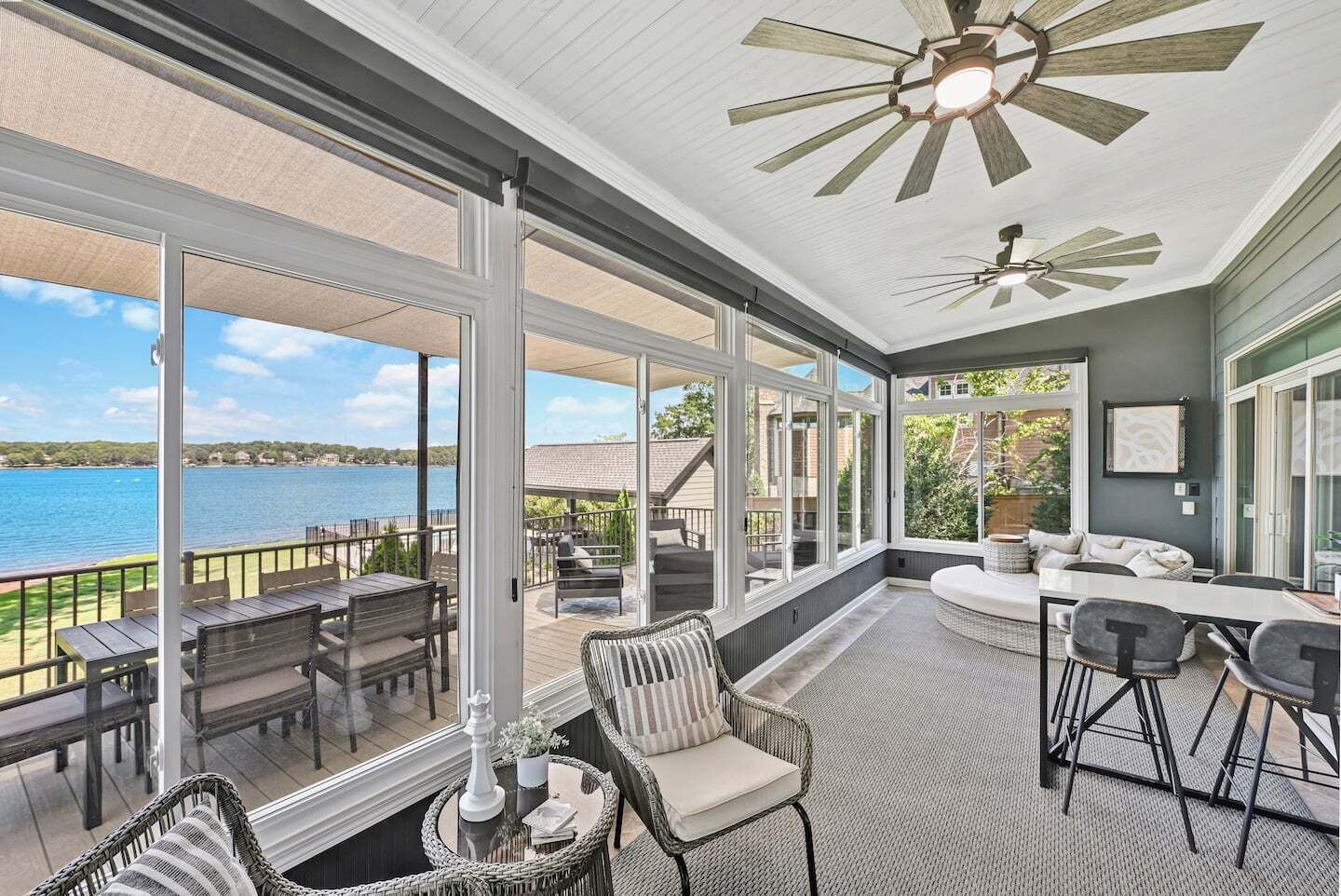 A covered outdoor area with a view of a lake, furnished with chairs and tables, and a ceiling fan.