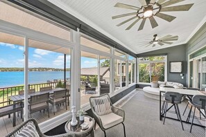 A covered outdoor area with a view of a lake, furnished with chairs and tables, and a ceiling fan. - Channel Marker: Exclusive Lakefront Home w/Hot Tub, Custom Bunk Room, Dock & Optional Boat Rental (Mooresville)