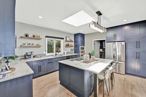 A modern kitchen with dark cabinetry, a central island, and a large window. - Channel Marker: Exclusive Lakefront Home w/Hot Tub, Custom Bunk Room, Dock & Optional Boat Rental (Mooresville)