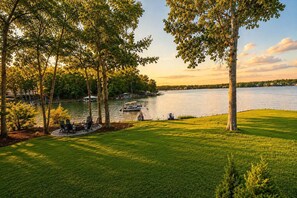 A lakeside property with a grassy lawn, trees, and a dock with boats. - Channel Marker: Exclusive Lakefront Home w/Hot Tub, Custom Bunk Room, Dock & Optional Boat Rental (Mooresville)