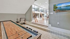 Une table de jeu de palet avec des zones numérotées à chaque extrémité, un fauteuil confortable et un téléviseur diffusant un paysage pittoresque.