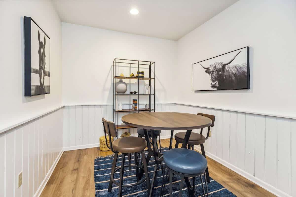 Een eetgedeelte met een ronde tafel, zes stoelen, een blauw vloerkleed en twee kunstwerken aan de muur.