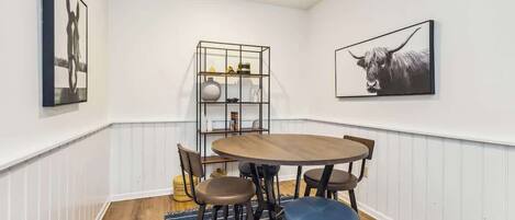 Een eetgedeelte met een ronde tafel, zes stoelen, een blauw vloerkleed en twee kunstwerken aan de muur.