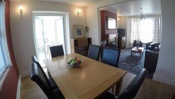A dining area with a wooden table and black chairs, a fruit bowl on the table, and a television in the background.