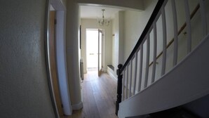 Ein Flur mit Holzboden, der zu einer Treppe mit weißen Geländern und einem schwarzen Handlauf führt.