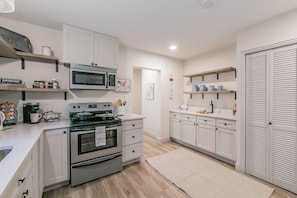 A modern kitchen with white cabinets, stainless steel appliances, and wooden flooring. - Charming Home Near Dickies+Free Biweekly Clean+KING Bed+Fully Furnished (Fort Worth)