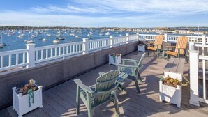 Une terrasse en bois, agrémentée de chaises Adirondack et de jardinières, donnant sur une marina où sont amarrés de nombreux bateaux.