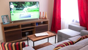 A living room with a television displaying a golf game, a wooden coffee table, and two sofas with striped cushions. - Duplex Equipped, with daily cleaning service  (Malargüe)