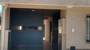 A building with a large garage door, a metal balcony, and a small window with a mesh screen. - Duplex Equipped, with daily cleaning service  (Malargüe)