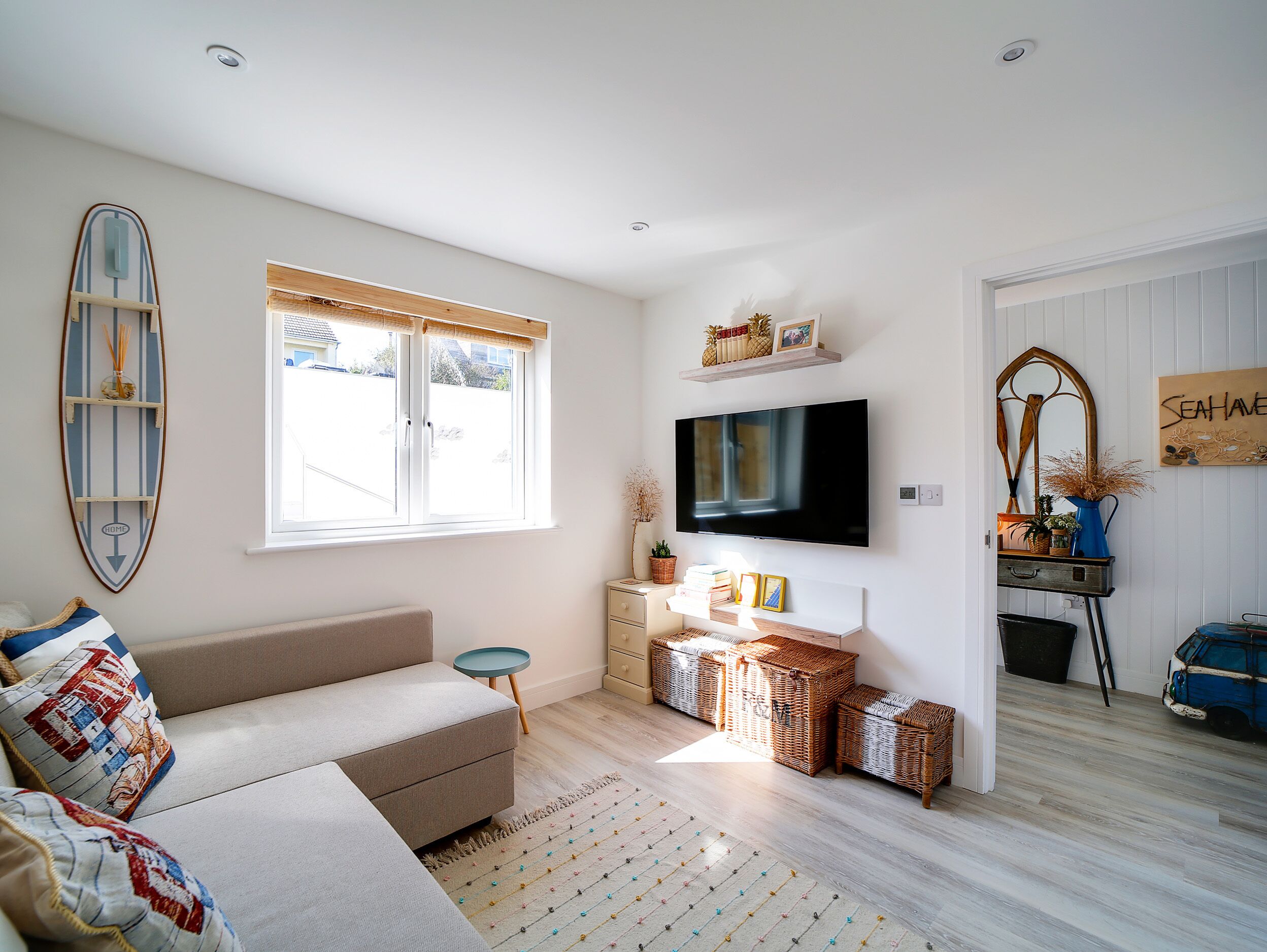 A modern living room with a sofa, a television, wicker baskets, and a surfboard decoration.