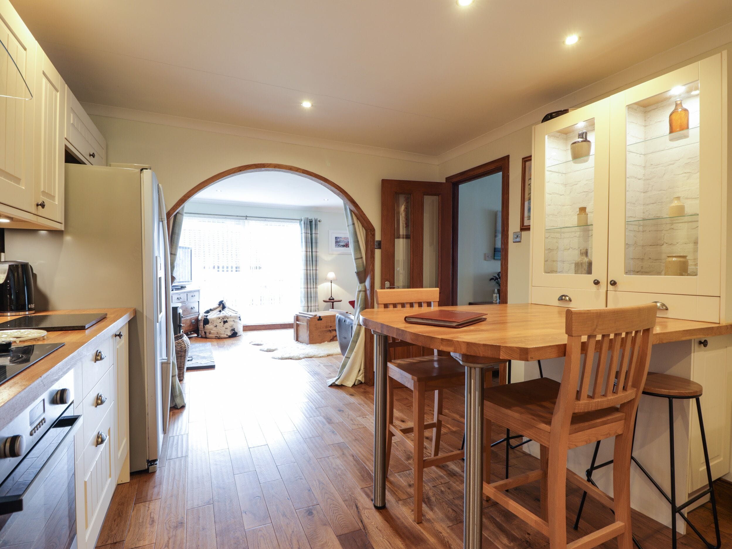 Una cocina con armarios de madera, una mesa de comedor con sillas y vistas a un salón a través de un arco.