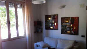 A room with a white sofa, a dining table with a bowl, and two abstract paintings on the wall. - Apartment from helium (La Caletta)