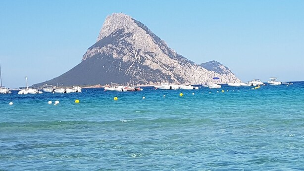 A coastal scene with a prominent rocky mountain in the background and several boats anchored in the water. - Apartment from helium (La Caletta)