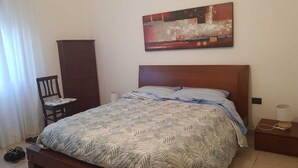 A bedroom with a bed, a chair, a wardrobe, and a painting on the wall. - Apartment from helium (La Caletta)