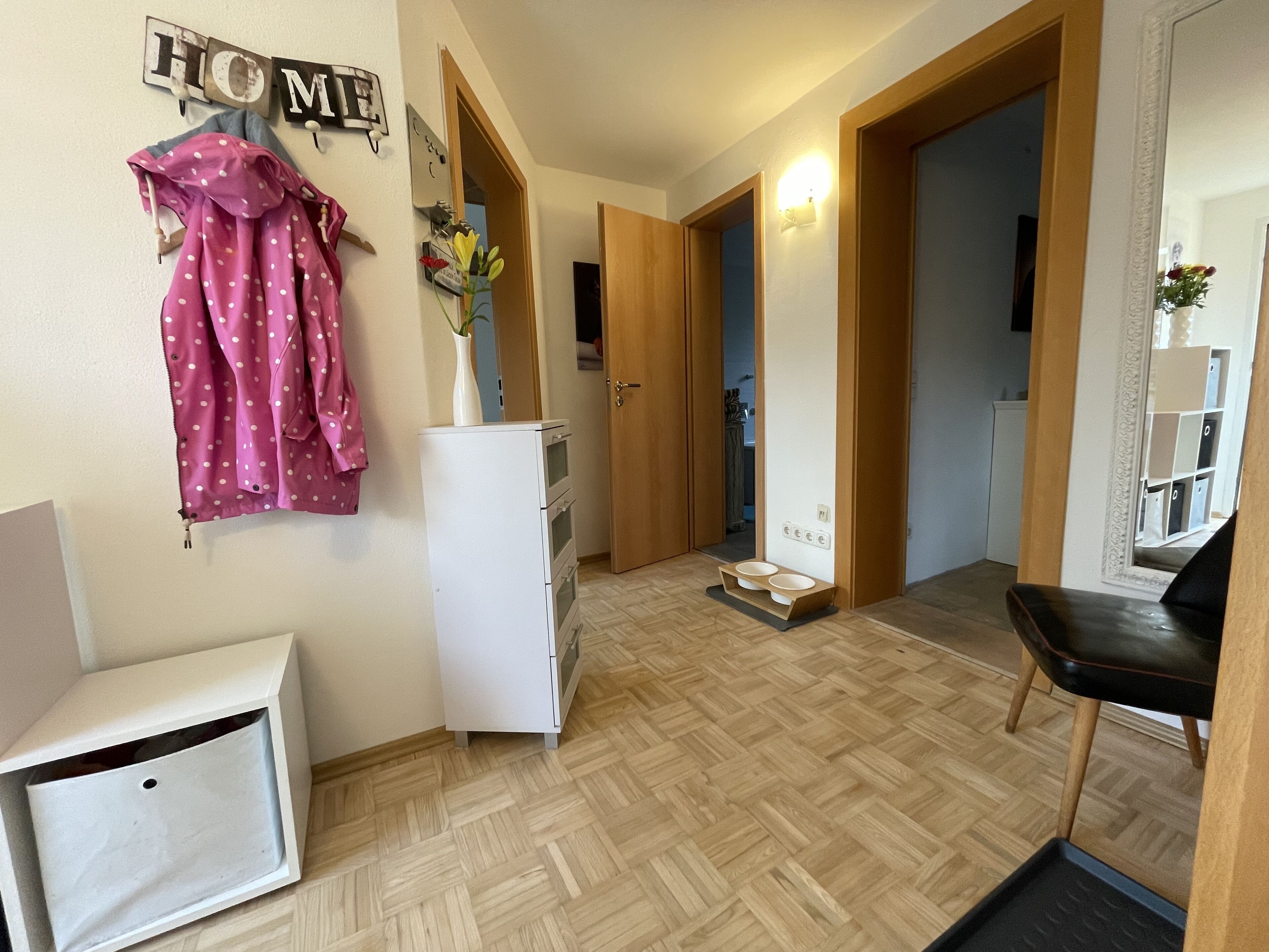Corredor com geladeira, piso de madeira, comedouro para animais de estimação e espelho com moldura decorativa.