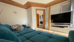 Un salon moderne avec un canapé de couleur turquoise, un téléviseur à écran plat et un plafond en bois.
