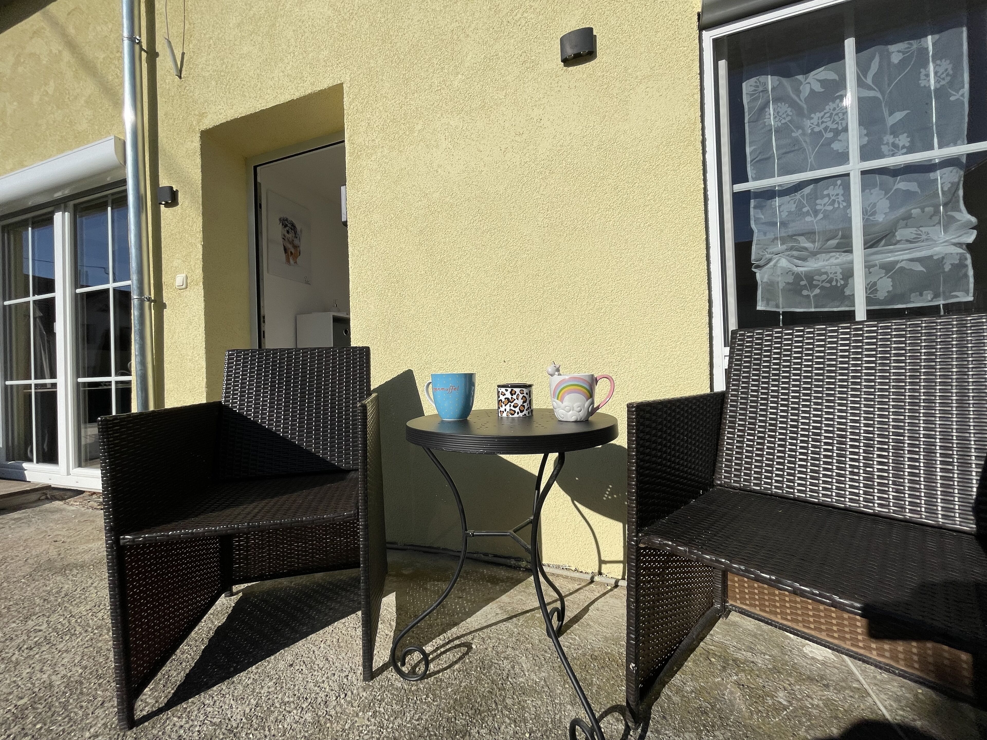 A patio area with two wicker chairs, a small round table, and two coffee mugs.