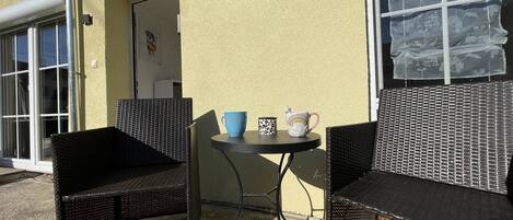 A patio area with two wicker chairs, a small round table, and two coffee mugs.
