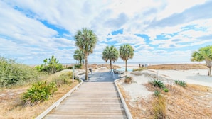 A wooden boardwalk leading to a beach area with palm trees and a sandy path. - Village House by Hilton Head Retreats (Hilton Head Island)