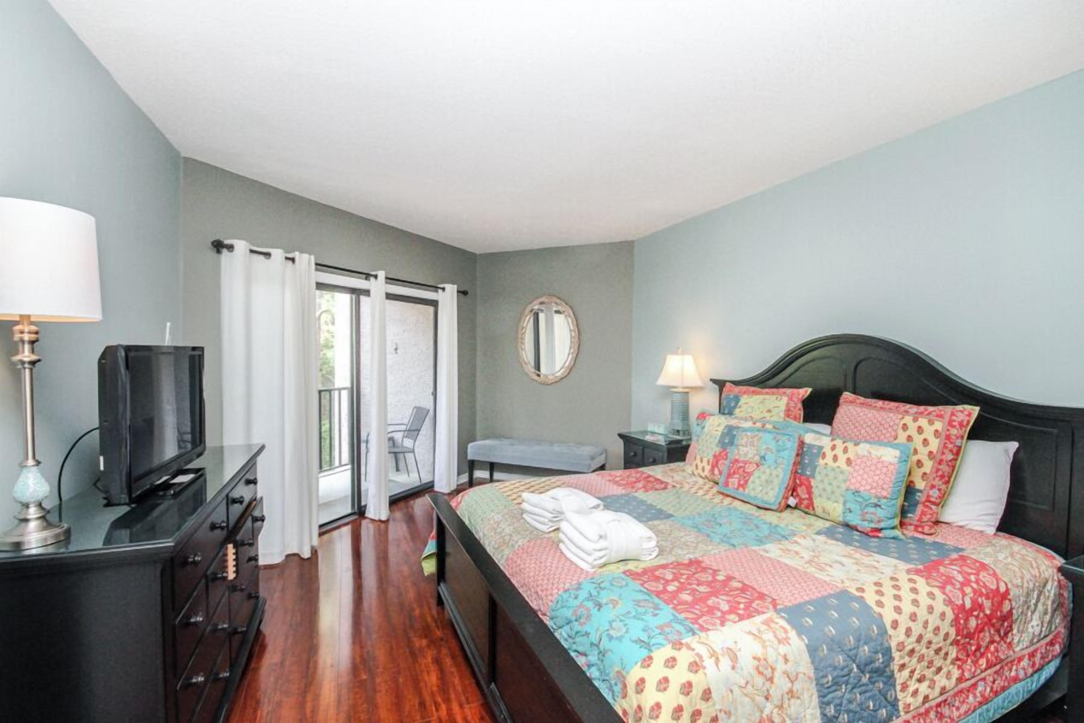 A bedroom with a bed, a television, a desk, a chair, a bench, and a window with curtains.