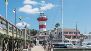 A pier with a lighthouse, boats, and a building with multiple flags. - Village House by Hilton Head Retreats (Hilton Head Island)