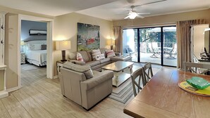A spacious living area with a sofa, a dining table, and a view of the outdoors through large sliding glass doors. - Village House by Hilton Head Retreats (Hilton Head Island)