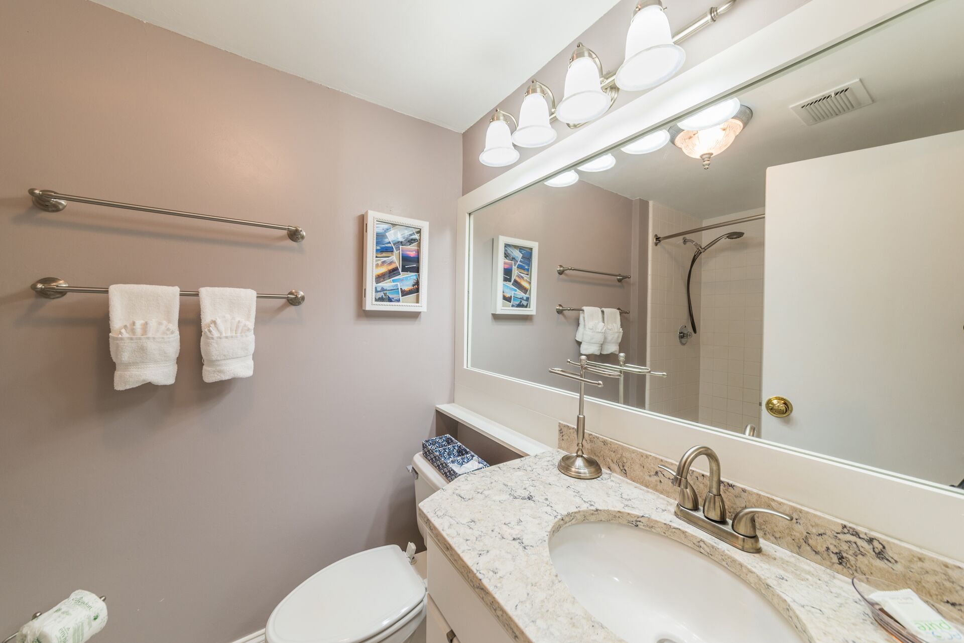 A bathroom with a large mirror, a sink with a marble countertop, and two towel racks with white towels.