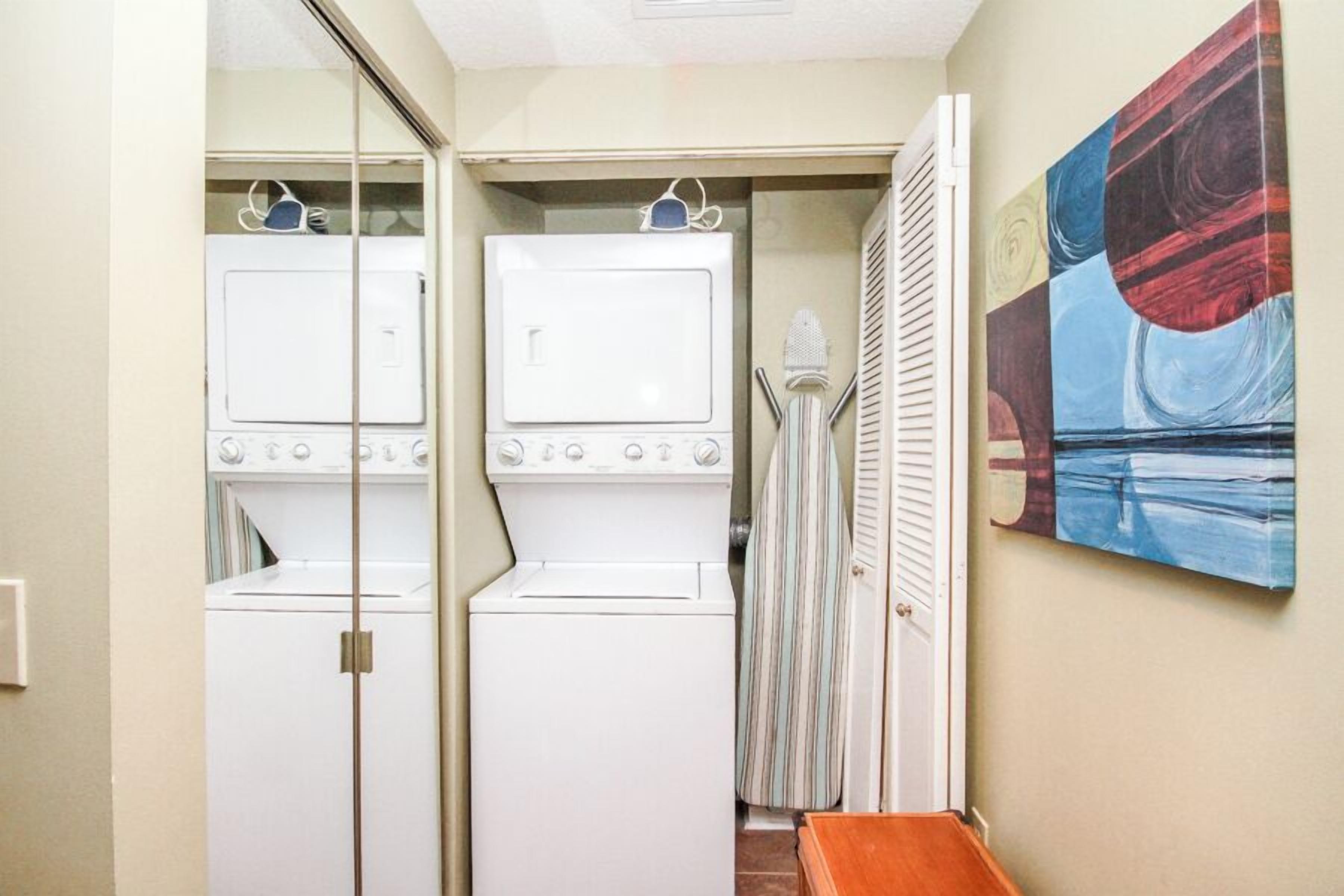 A laundry room with two stacked washers and dryers, a striped shower curtain, and a painting on the wall.