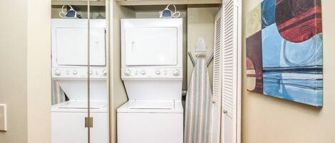 A laundry room with two stacked washers and dryers, a striped shower curtain, and a painting on the wall.