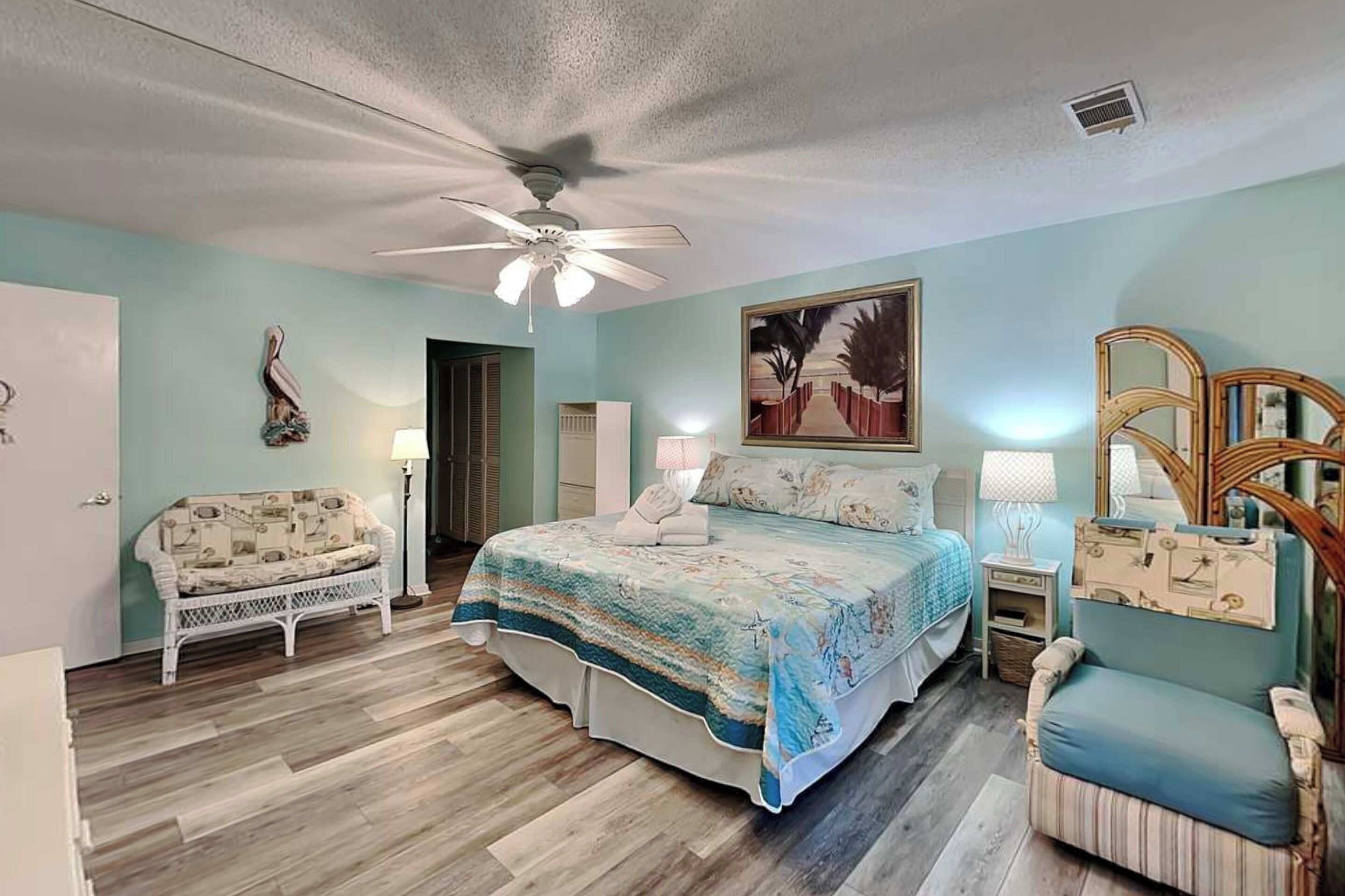 A bedroom with a bed, a chair, a desk, a ceiling fan, and a painting on the wall.