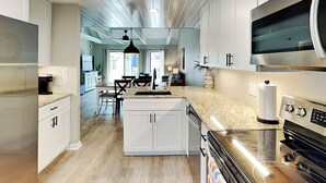 A modern kitchen with white cabinetry, a central island, stainless steel appliances, and a dining area with a chandelier. - Queens Grant by Hilton Head Retreats (Hilton Head Island)