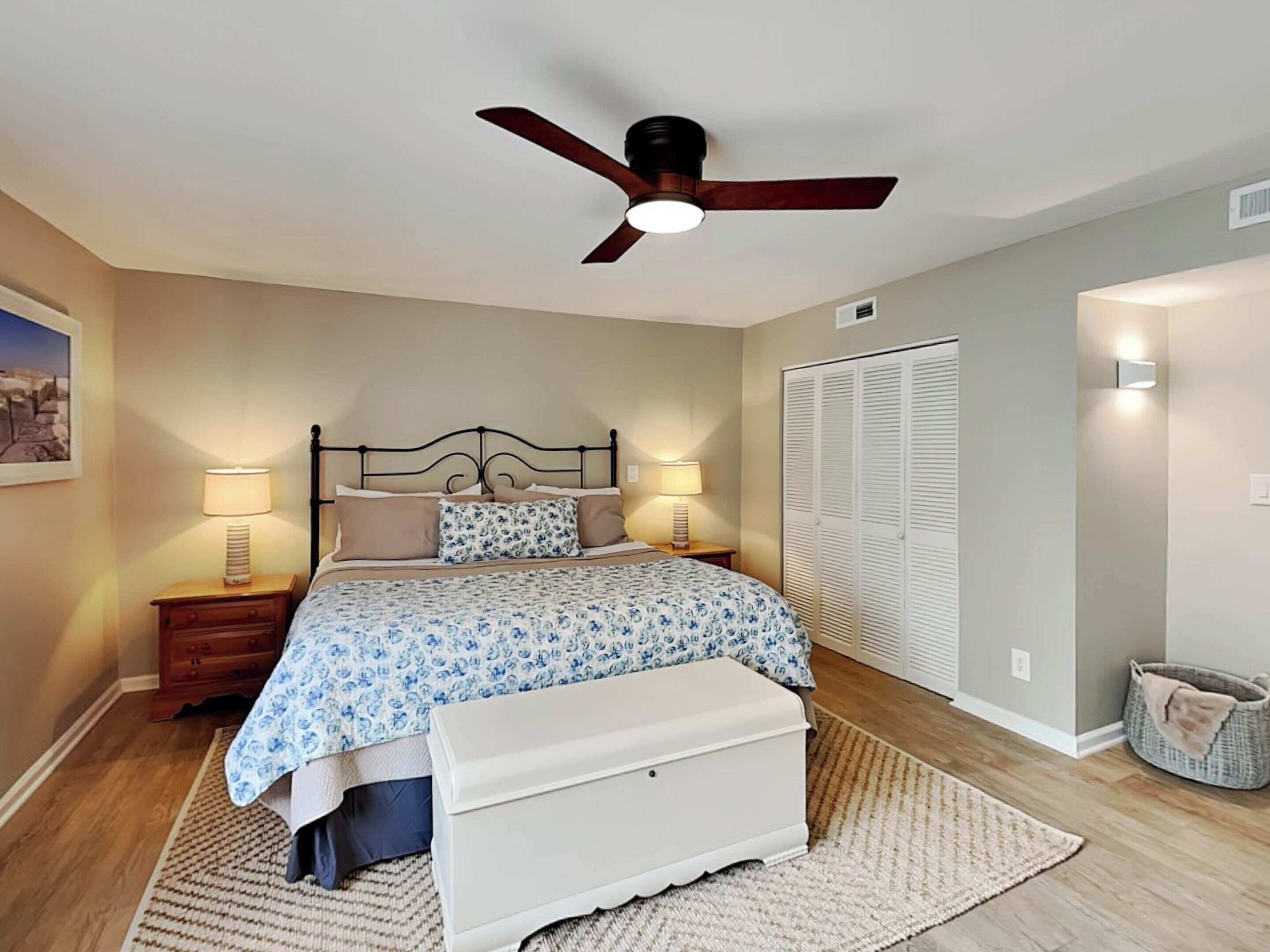 A bedroom with a bed, bedside lamps, a ceiling fan, a wardrobe, and a small rug.