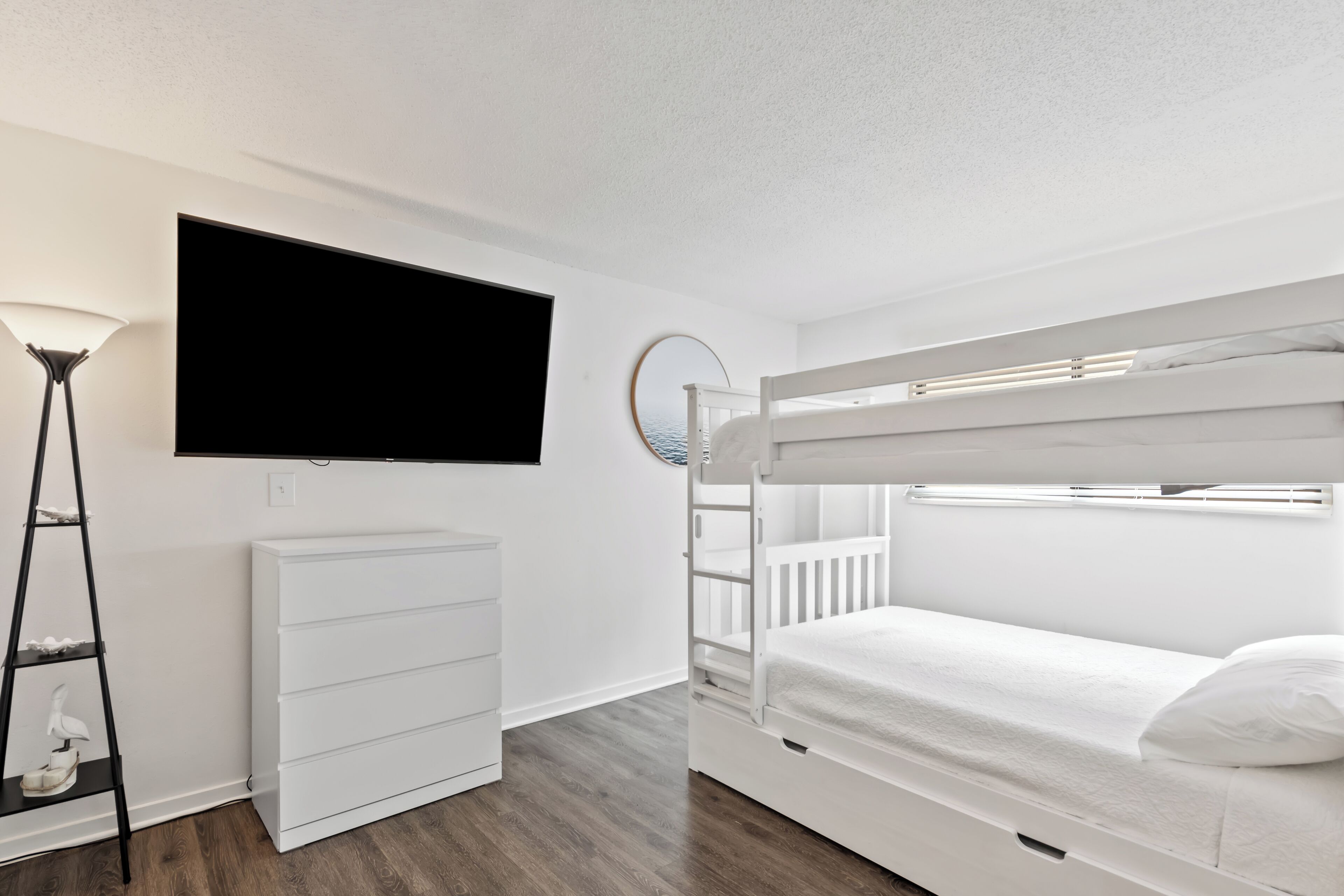 A modern bedroom with a bunk bed, a flat-screen TV, a white dresser, and a ladder.