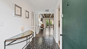 A hallway with a glass table, a vase with flowers, and a green door. - Queens Grant by Hilton Head Retreats (Hilton Head Island)