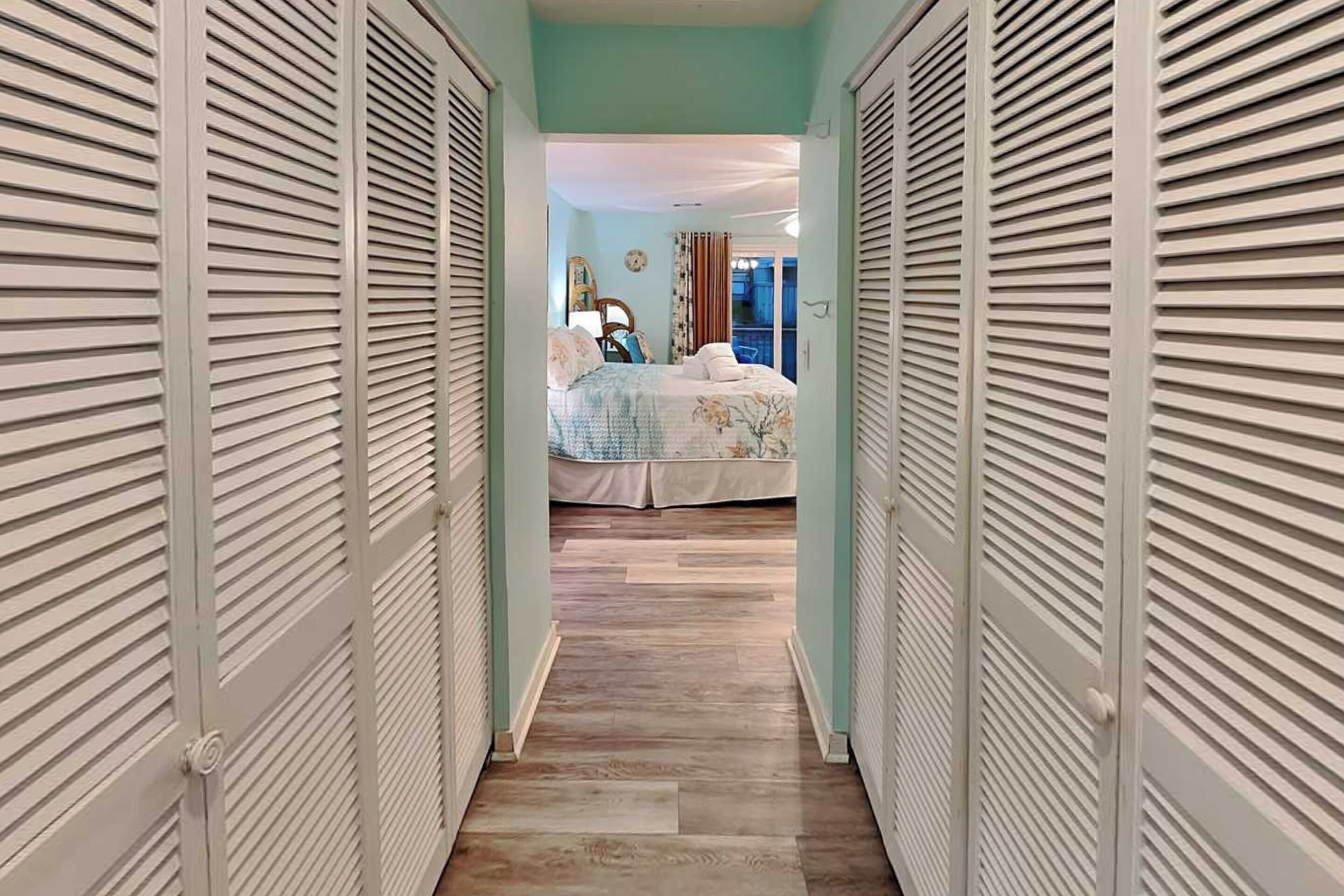 A hallway leading to a bedroom with a bed, a dresser, and a mirror.
