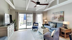 A spacious living room with a large flat-screen TV, a ceiling fan, a sofa, a coffee table, and a painting on the wall. - Queens Grant by Hilton Head Retreats (Hilton Head Island)