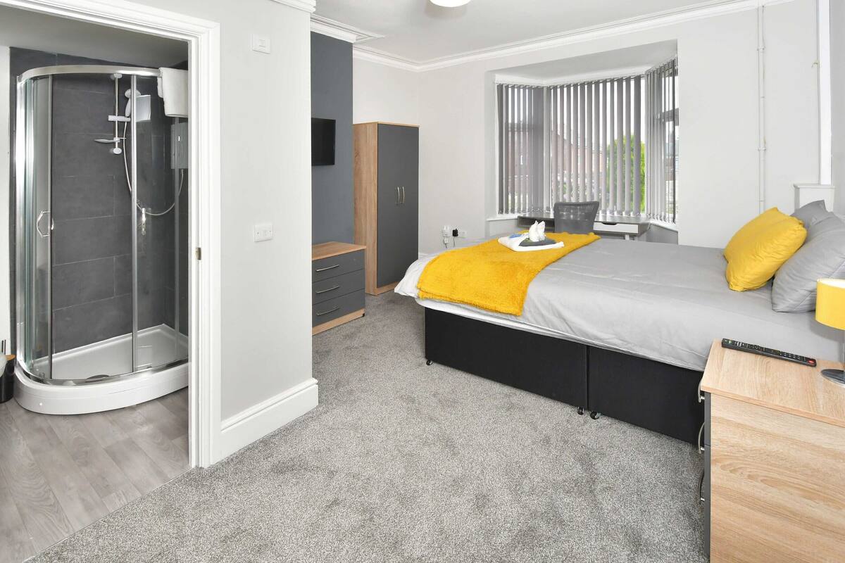 Un dormitorio moderno con cama, mesita de noche, persianas y zona de ducha.