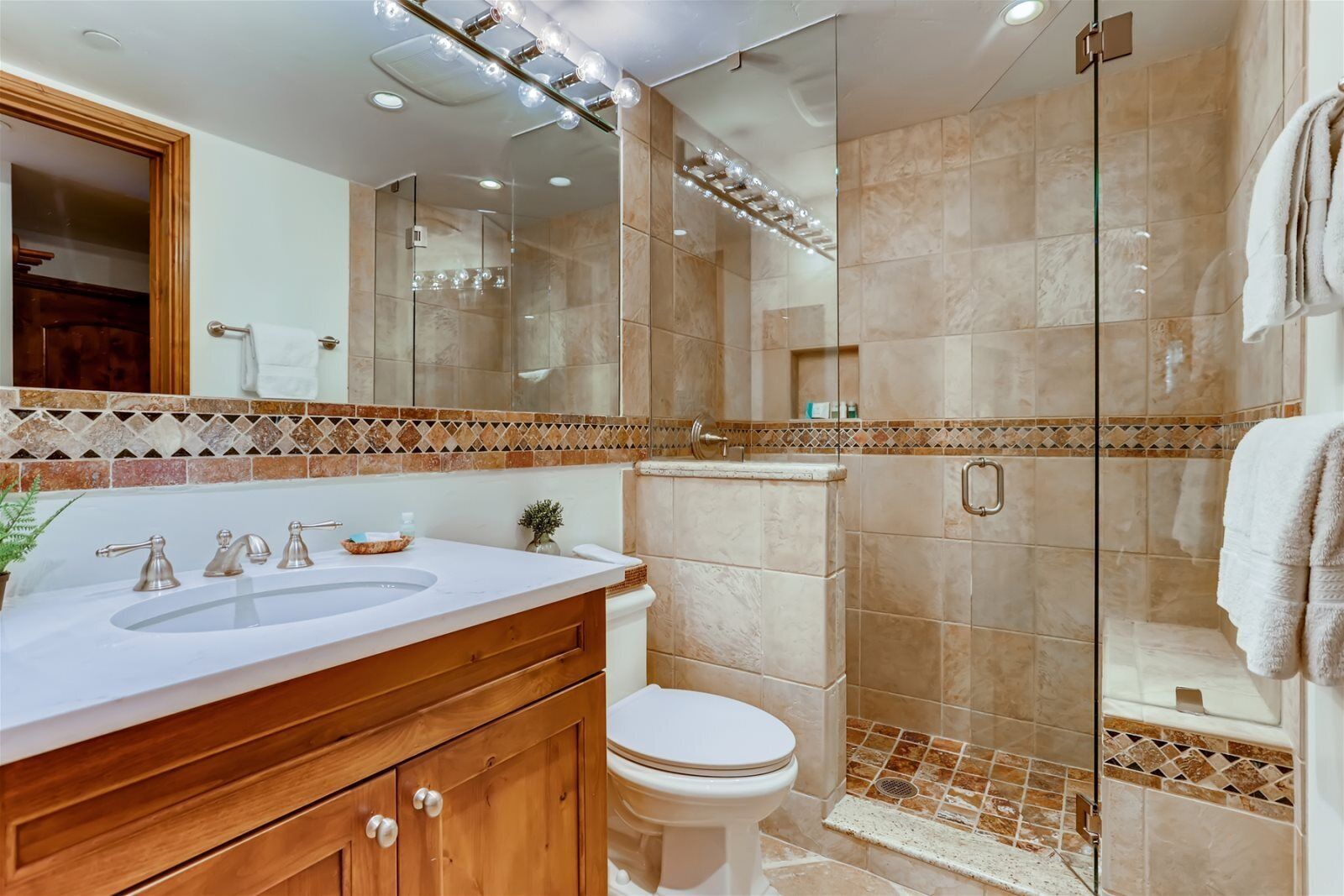 A modern bathroom with a glass-enclosed shower, a white sink with a wooden vanity, and a large mirror.