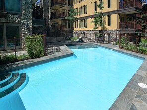 A swimming pool with stone steps leading into it, surrounded by a stone wall and a fence. - Village Center Condo 4J (Vail)