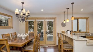 A spacious dining area with a wooden table and chairs, a chandelier, and a view through large glass doors to an outdoor deck. - Potato Patch (Vail)