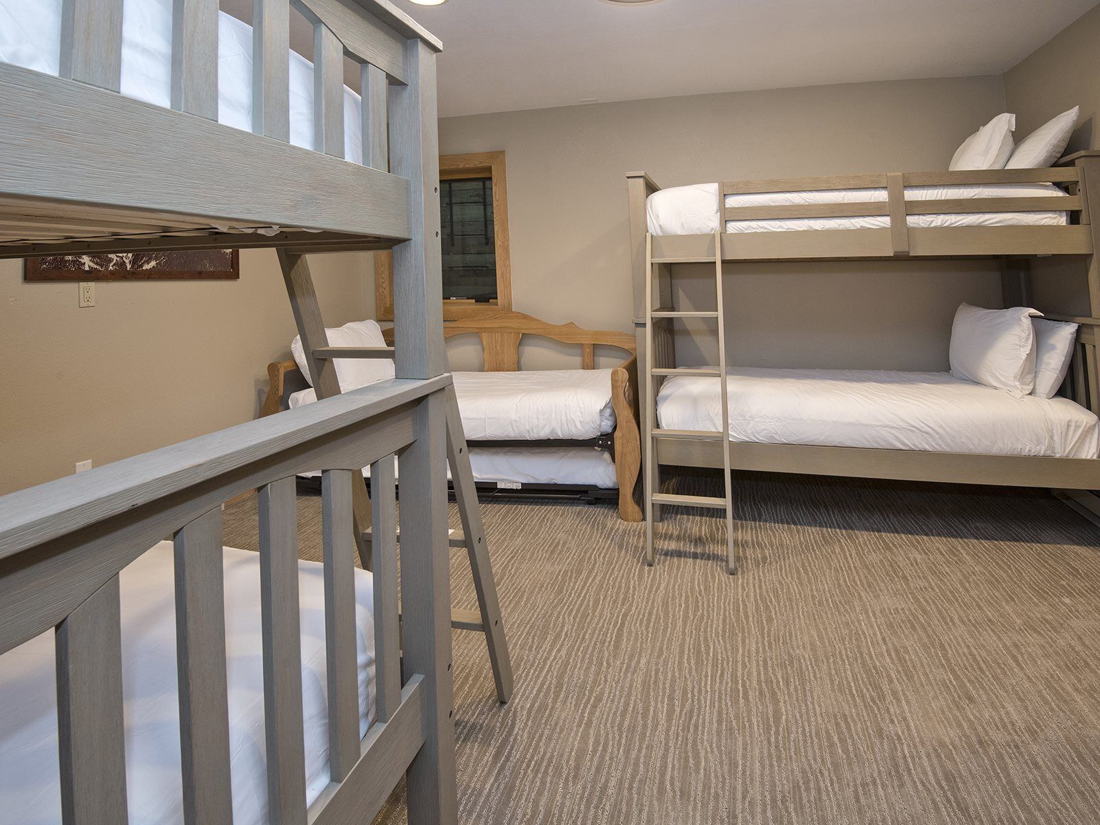 A bunk bed room with a wooden ladder, a small desk, and a window.