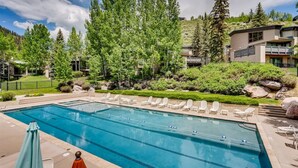 A rectangular swimming pool with clear blue water, surrounded by lounge chairs and a well-maintained garden with various shrubs and trees. - Potato Patch (Vail)