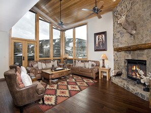 A cozy living room with a stone fireplace, leather furniture, and a large window overlooking a snowy landscape. - Potato Patch (Vail)