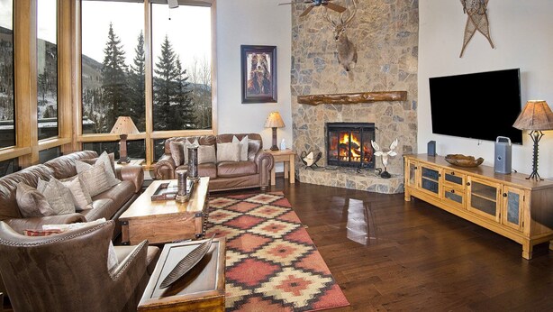 A cozy living room with a stone fireplace, leather furniture, and a large window offering a view of trees. - Potato Patch (Vail)