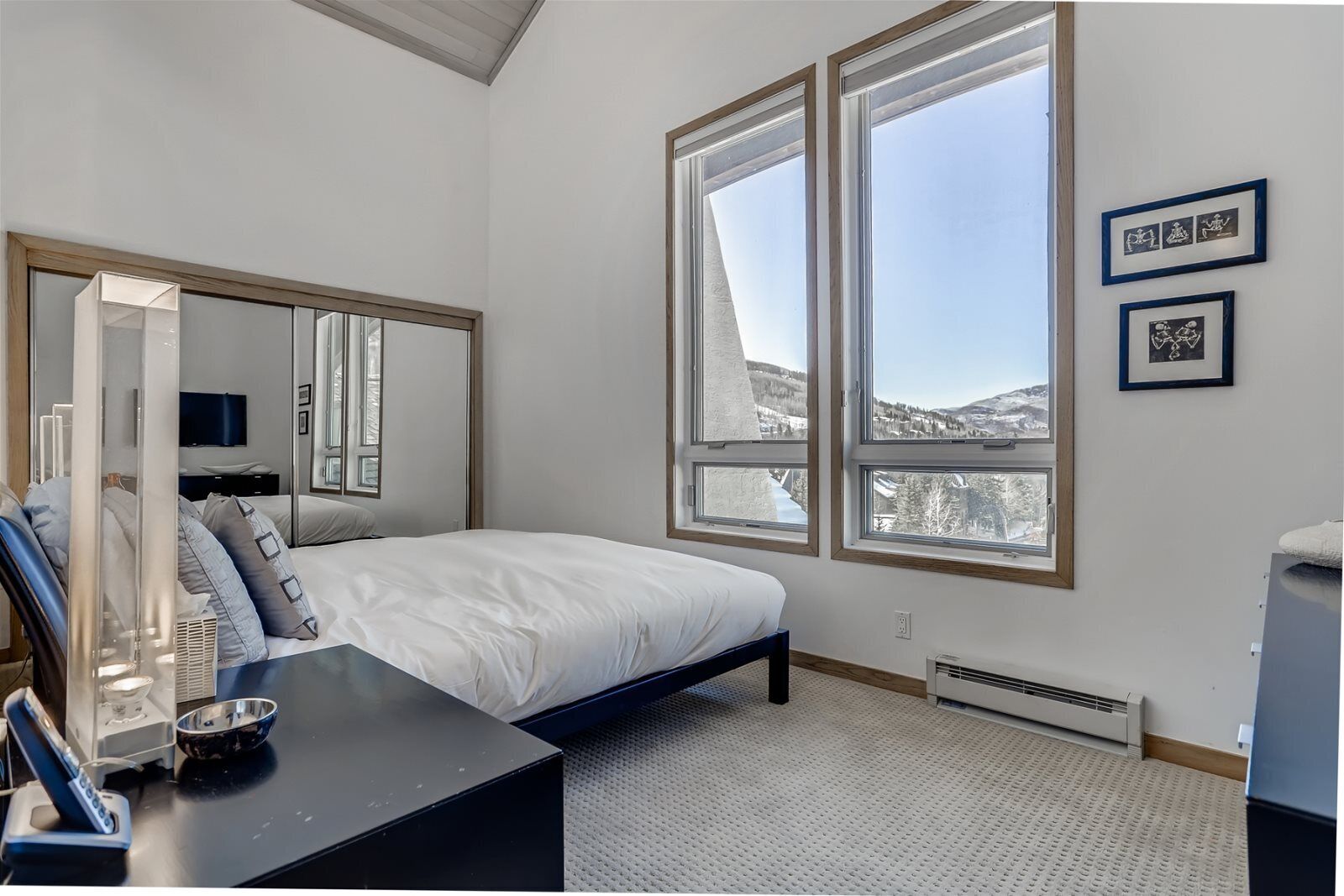 A bedroom with a large bed, a bedside table, a mirror, and a window with a mountain view.