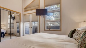 A bedroom with a large bed, a TV mounted on the wall, and a view of the outside through the window. - Tyrolean 6 (Vail)
