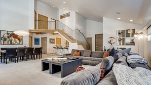 A spacious living area with a large sofa, a dining table, and a staircase leading to an upper level. - Tyrolean 6 (Vail)
